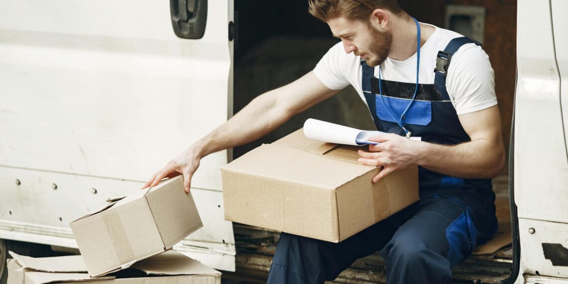 Man in uniform sorts packages by a white van, emphasizing efficient delivery service.