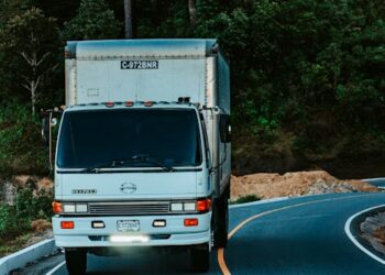 A white truck driving on a winding road surrounded by dense green forest plants.